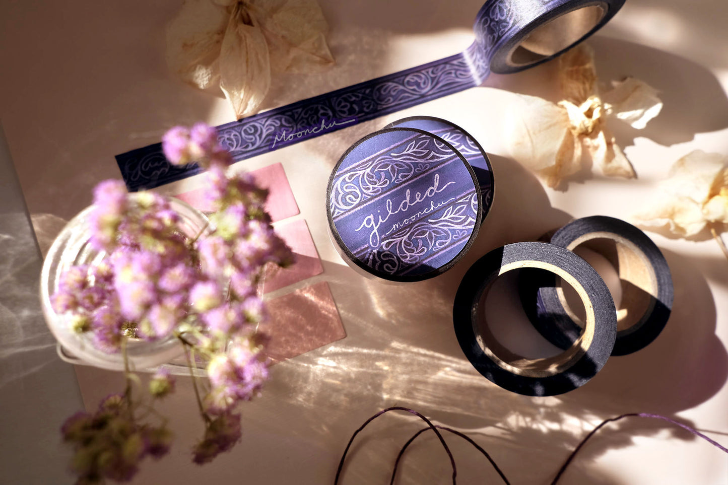 photo depicts original artist washi tape by moonchu. this design was created in watercolour, and transformed into washi tape for your journals, bujos, hobonichis, crafts, etc. it is a beautifully ornate design with swirls and leaves, swathed in a deep purple and navy background. the design itself is a light purple-ish colour. very art nouveau/filigree, large library with tons of amazing smelling books inspired. elaborate washi tape design.