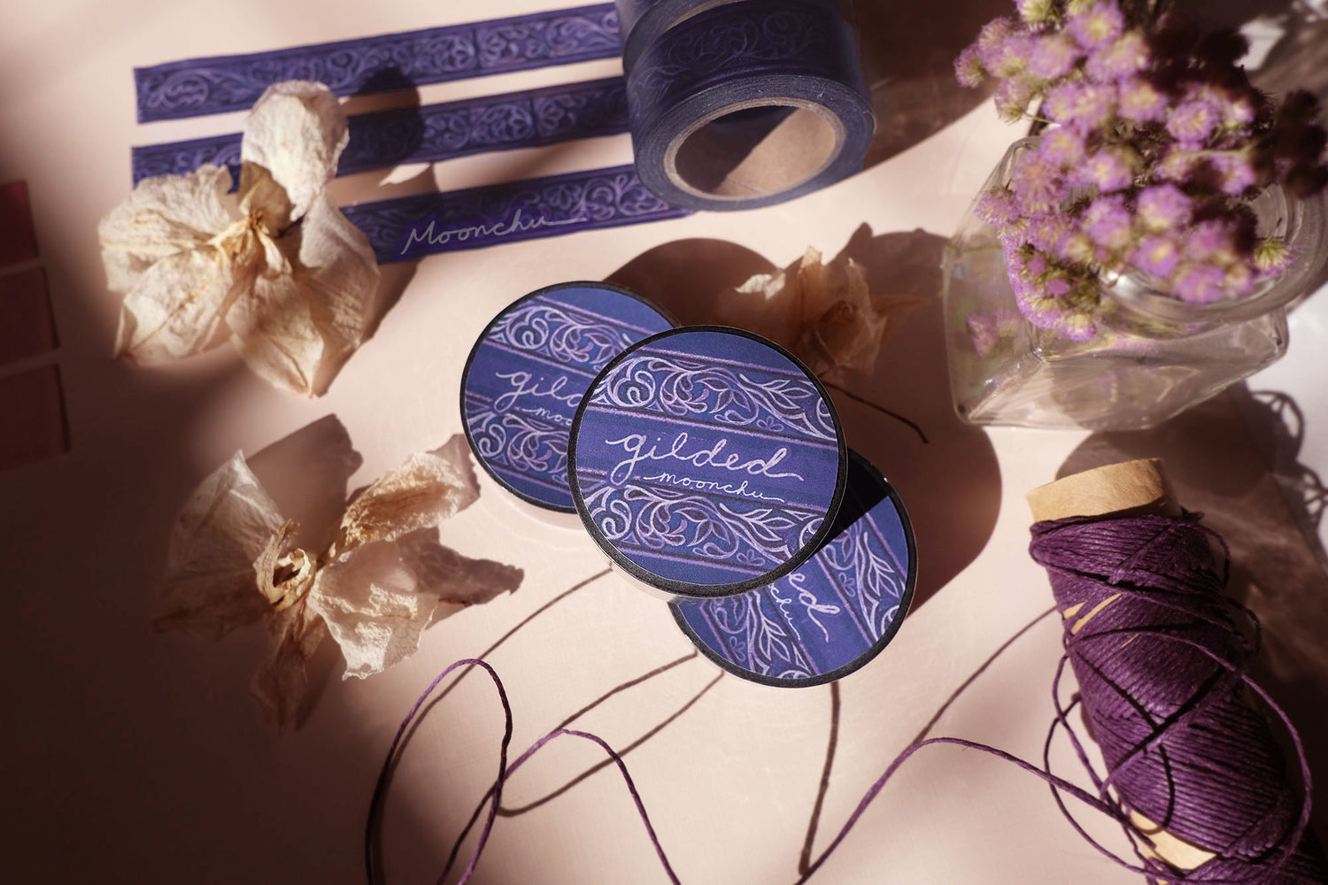 photo depicts original artist washi tape by moonchu. this design was created in watercolour, and transformed into washi tape for your journals, bujos, hobonichis, crafts, etc. it is a beautifully ornate design with swirls and leaves, swathed in a deep purple and navy background. the design itself is a light purple-ish colour. very art nouveau/filigree, large library with tons of amazing smelling books inspired. elaborate washi tape design.