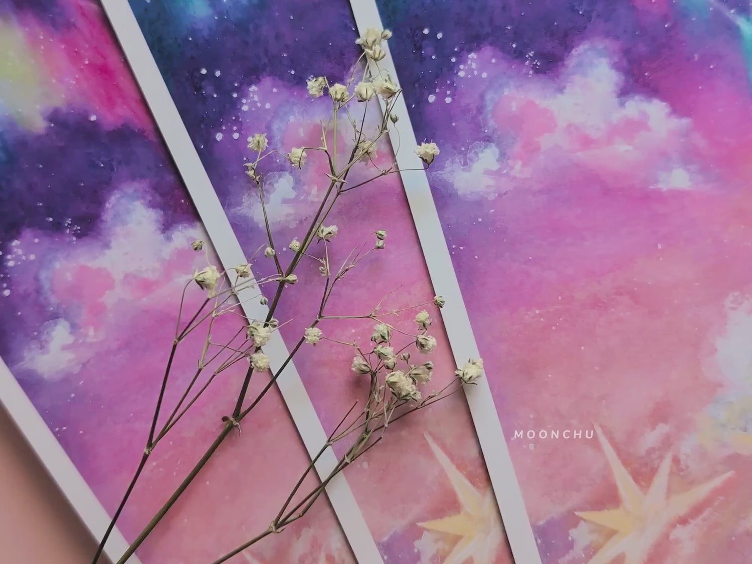 a video showcasing original painting by moonchu. features pink writing utensils, dried baby's breath flowers, and high quality art print. illustrates details and colour and quality of the painting recreation.