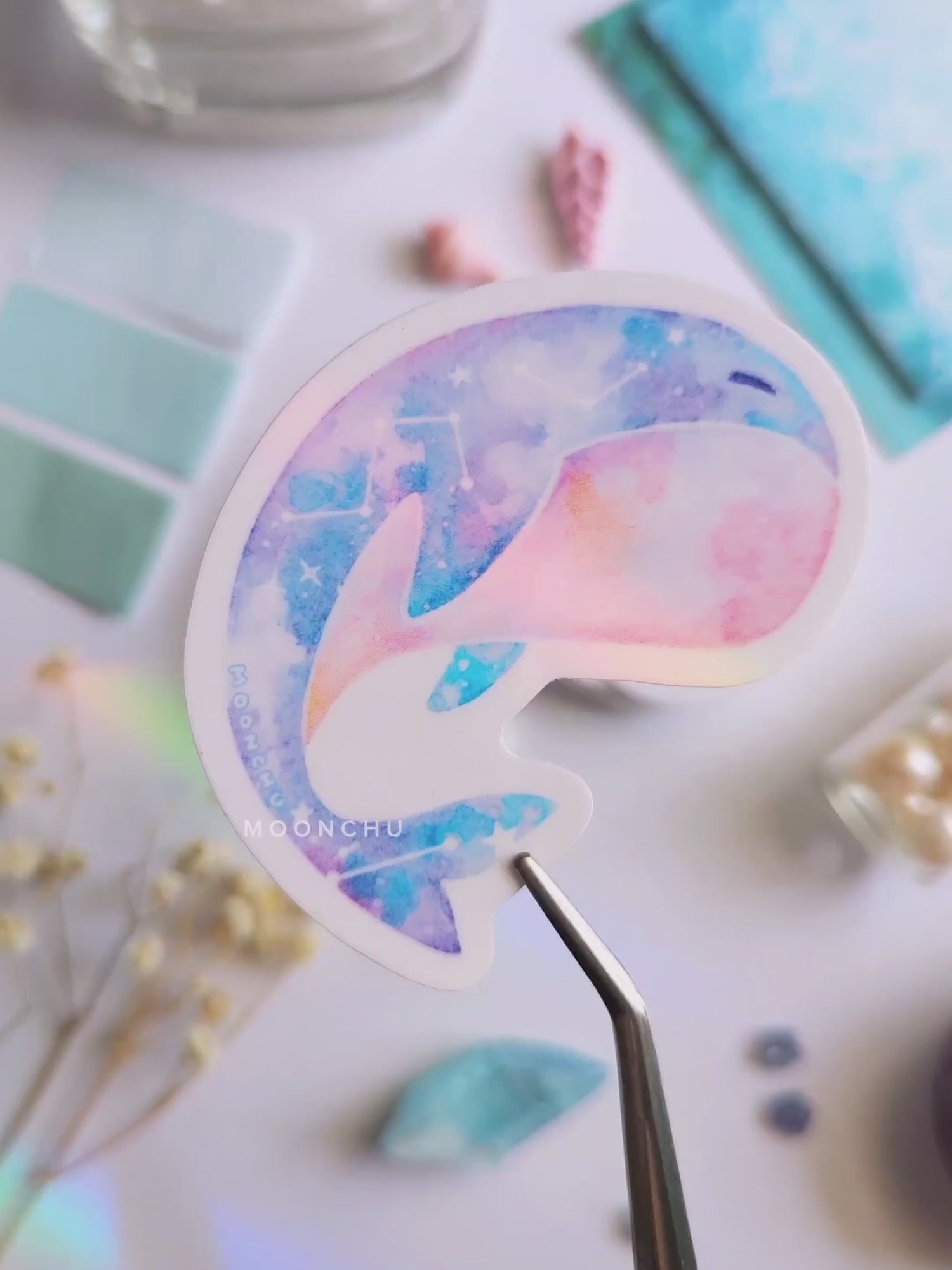 video showcases a watercolour painted calming whale sticker! original illustrated ocean art. flatlay consists of other ocean items, like little shells and pearls. a high quality vinyl sticker for shark lovers or ocean gifts. perfect sticker for shark week.