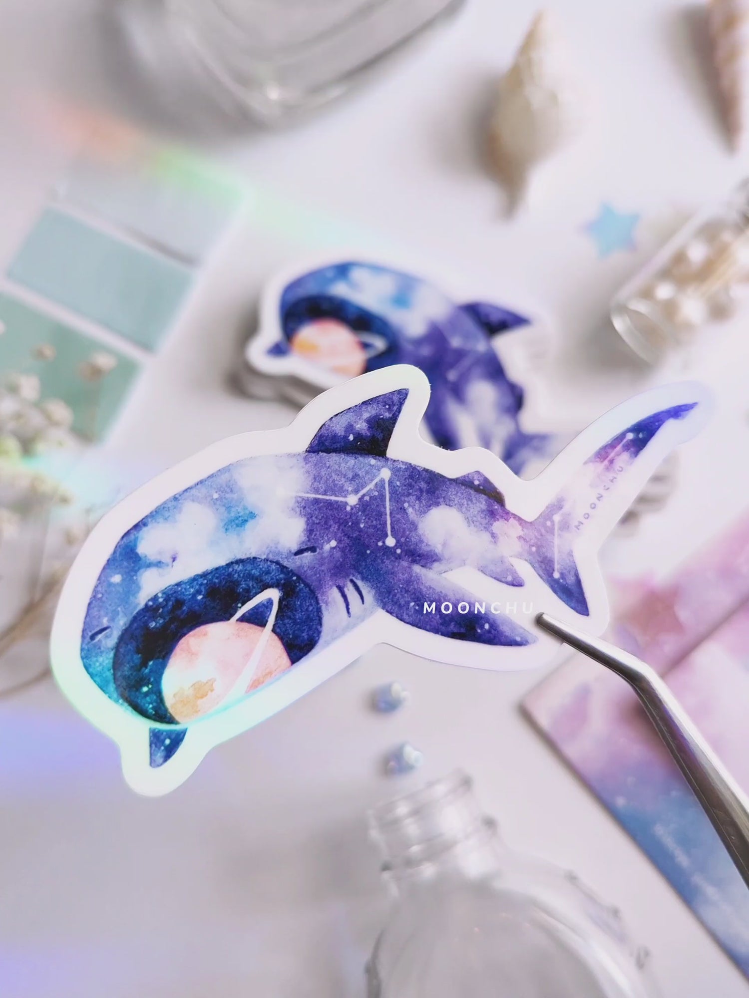 video showcases high gloss vinyl sticker of original megamouth shark illustration. flatlay consists of other ocean items, like little shells and pearls. a high quality vinyl sticker for shark lovers or ocean gifts. perfect sticker for shark week.