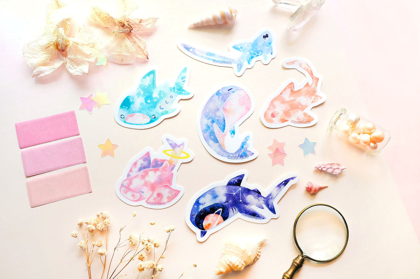 original art illustrated stickers by moonchu depicting watercolour painted sharks! this little ocean creature collection consists of a thresher shark, a whale shark, a whale, an angel shark, a leopard shark, and a megamouth shark. all vibrantly coloured and celestial themed high quality stickers! flatlay consists of other ocean items, like little shells and pearls. a wonderful gift for shark lovers or ocean enjoyers. perfect sticker for shark week.