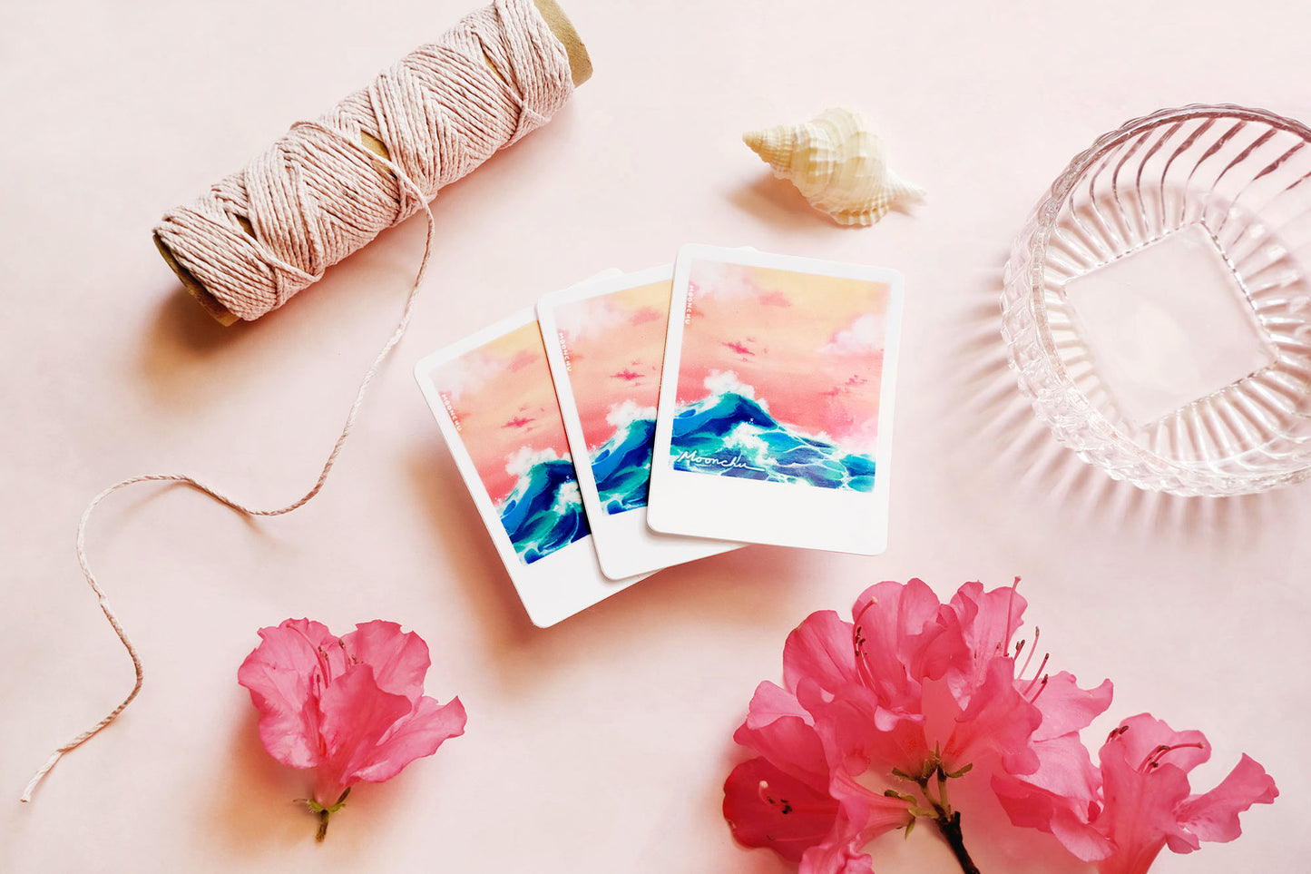 product image showcasing moonchu's original art sticker depicting a beautiful orange sunset and a teal wave with a white border, like a printed snapshot. a super glossy and saturated high quality vinyl sticker of ocean wave sunset. various stationery items, dried florals, and seashells adorn the image. a unique sticker for any ocean lover or beach goer. would look great on a water bottle that you take to the beach during the summer!