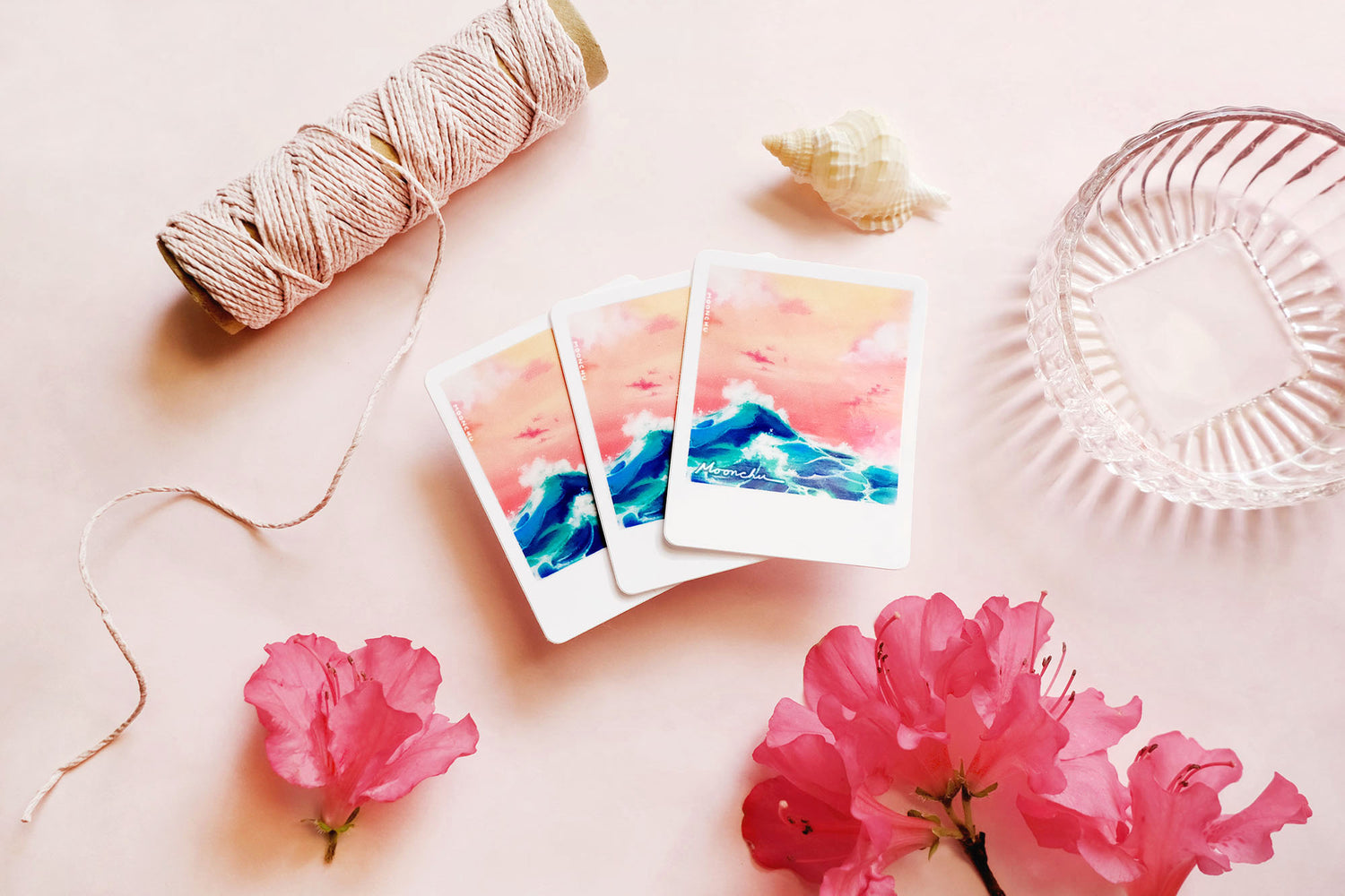 product image showcasing moonchu's original art sticker depicting a beautiful orange sunset and a teal wave with a white border, like a printed snapshot. a super glossy and saturated high quality vinyl sticker of ocean wave sunset. various stationery items, dried florals, and seashells adorn the image. a unique sticker for any ocean lover or beach goer. would look great on a water bottle that you take to the beach during the summer!