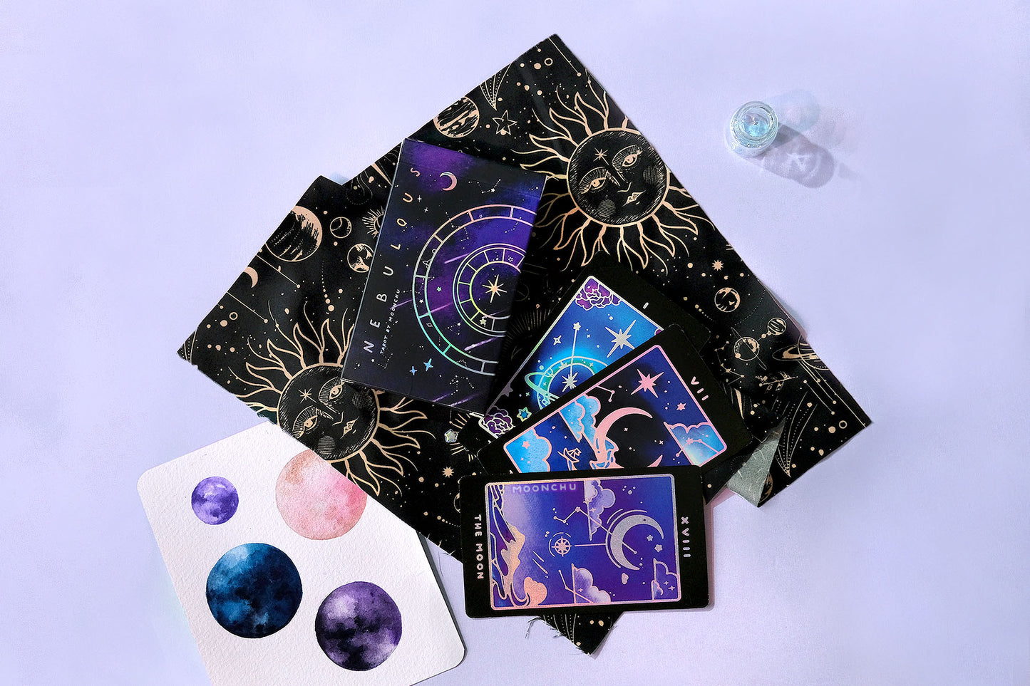 indie tarot deck by moonchu, all original art designs! featuring several magical nature and animal themed tarot cards. the magician is an ouroboros teal snake with a ring around him like a planet along with constellations. the chariot features a large crescent moon with a little sailboat floating along, amongst starry clouds. the third card is the moon, a popular original tarot design with a crescent moon hung amongst clouds, constellations, above an ocean wave. all with holographic accents.