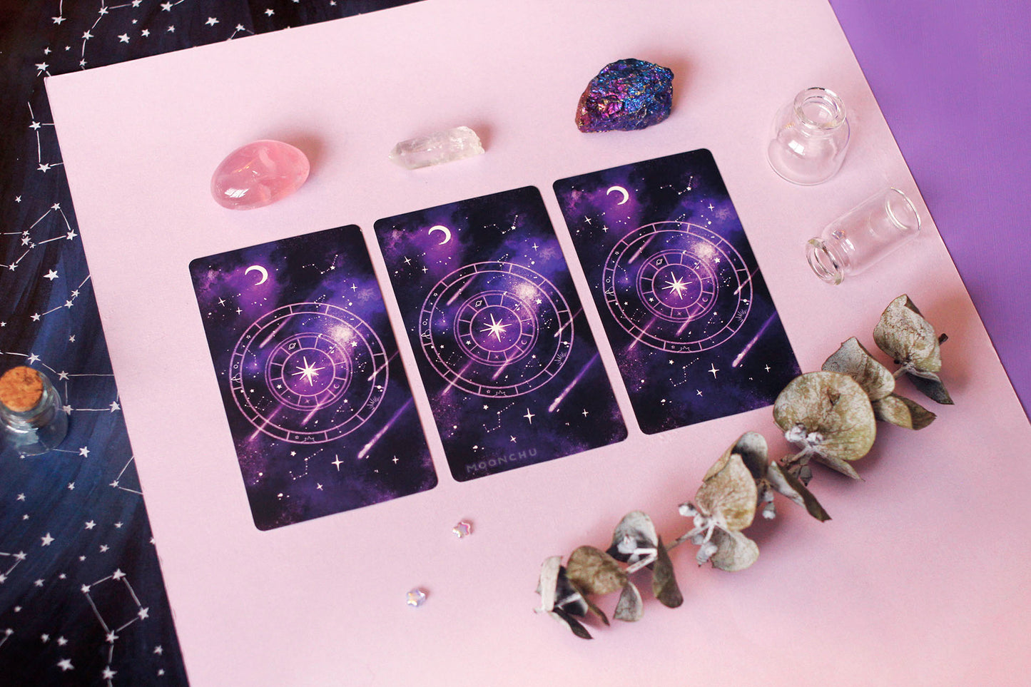 photo depicts the back of the nebulous arcana indie major arcana deck by moonchu. these were originally watercolour designs, with rich purple and black clouds illustrating space, along with constellations and shooting stars. a crescent moon hangs in the left corner, with the center drawn magical starry wheel. a twinkling star accents the center of the wheel.
