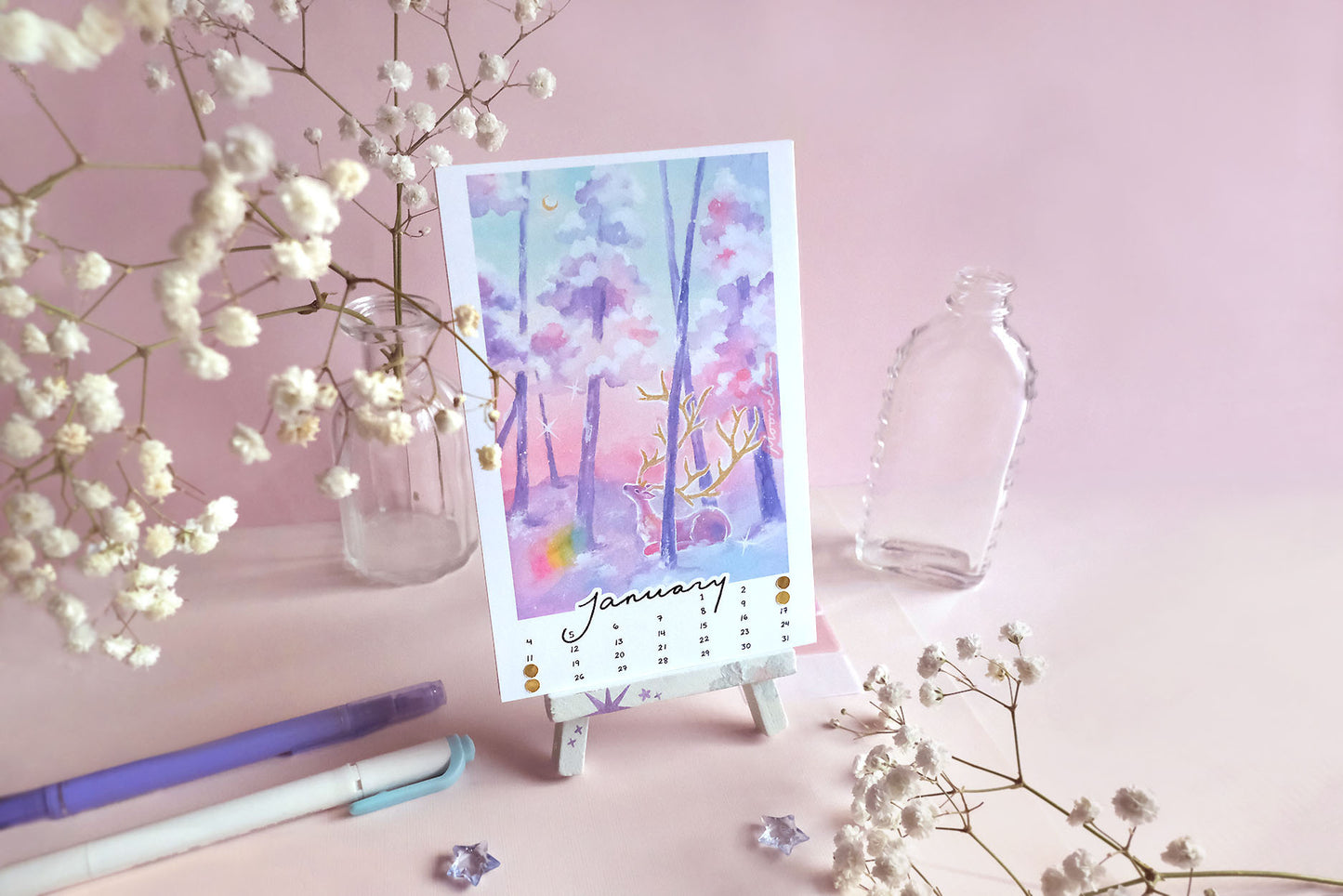 the month of january of the moonchu calendar. this original watercolour painting depicts a pink deer with large gold antlers sitting upon blue and purple snow, looking up towards a golden crescent moon in the sky. deer is nestled in purple forest of trees, with snow lying atop the tree branches. a rainbow orb floats in the bottom left of the painting. january is in cursive script at the bottom, hand-written numbers date the month. hand-placed golden circles notate the moon phases of the month. 
