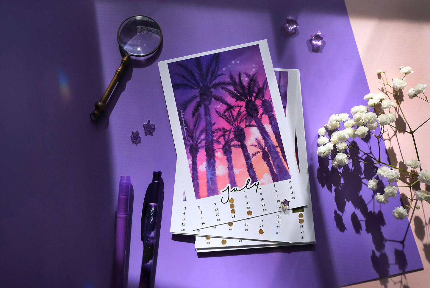 the month of july for the moonchu calendar. this original watercolour painting is comprised of a saturated purple, pink, orange gradient sunset seen through large, dark purple palm trees. palm trees have little stars on their trunks. clouds and constellations hang in the sky. july is in cursive script at the bottom, hand-written numbers date the month. hand-placed golden circles notate the moon phases of the month.