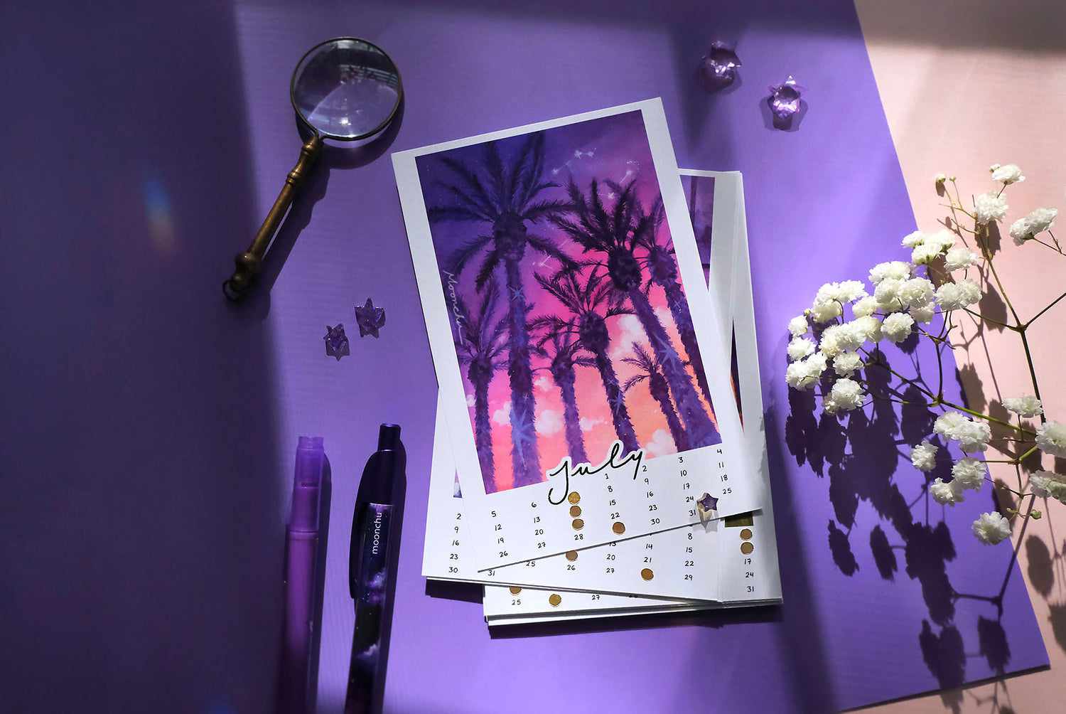 the month of july for the moonchu calendar. this original watercolour painting is comprised of a saturated purple, pink, orange gradient sunset seen through large, dark purple palm trees. palm trees have little stars on their trunks. clouds and constellations hang in the sky. july is in cursive script at the bottom, hand-written numbers date the month. hand-placed golden circles notate the moon phases of the month.