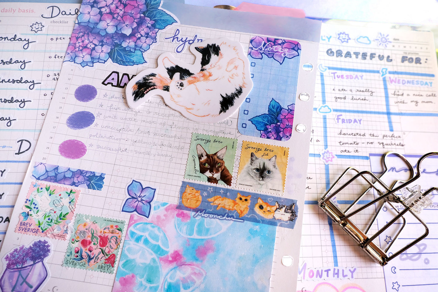 flatlay illustration full of random journal pages full of various original illustrated stickers by moonchu (hydrangeas, flowers) and memopad (jellybois memopad in the shop), moonchu cat washi tape, and the adorable calico cat nap stretch glossy vinyl sticker. a stationery feast for the eyes (mostly comprised of blues and some pops of orange).