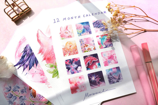 image depicts flatlay consisting of moonchu's original art calendar with thumbnail images of colourful and mystical moons for each month, as well as accompanying gold moon phase stickers and white stand. also dried flowers.