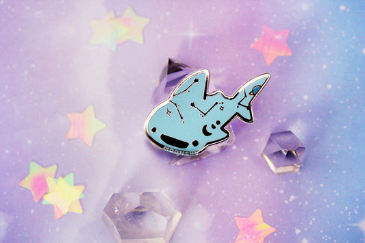 photo depicts original art enamel pin by moonchu of a very happy and serene celestial whale shark with constellations, moon phases, and a planet decorating its body. an enamel pin merging space lovers and ocean lovers alike.