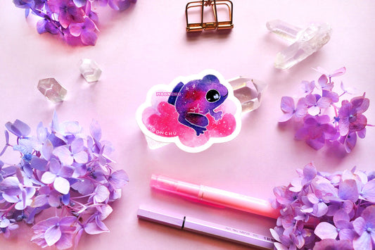 original watercolour painting by moonchu turned into a vinyl sticker! depicts a jammy grape magenta frog, smiling and sitting on a puffy pink cloud. he is looking to the right, maybe thinking about a snack. little stars are scattered amongst the sticker. quartz crystals and purple and blue hydrangea flowers litter a pink backdrop.