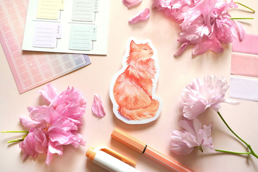 original illustrated sticker by moonchu of her fluffy orange kitty! painted in watercolours, this high quality vinyl sticker illustrates a regal, standing cat with his tail curled around his body. smiling, looking to his right. flatlay photo consists of pink stationery items and flowers. a sweet sticker for cat lovers and stationery lovers alike.