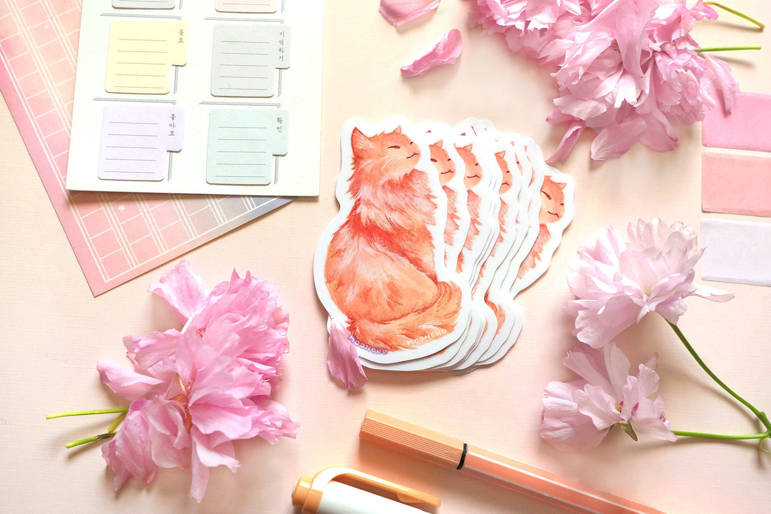 original illustrated sticker by moonchu of her fluffy orange kitty! painted in watercolours, this high quality vinyl sticker illustrates a regal, standing cat with his tail curled around his body. smiling, looking to his right. flatlay photo consists of pink stationery items and flowers. a sweet sticker for cat lovers and stationery lovers alike.