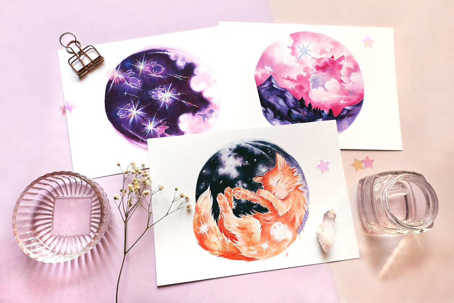 flatlay style photo of 3 original art pieces from moonchu's monthly moon series. has little stars, dried flower, and glass pieces as decor.