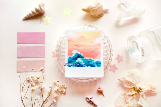 product image showcasing moonchu's original art sticker depicting a beautiful orange sunset and a teal wave with a white border, like a printed snapshot. a super glossy and saturated high quality vinyl sticker of ocean wave sunset. various stationery items, dried florals, and seashells adorn the image. a unique sticker for any ocean lover or beach goer. would look great on a water bottle that you take to the beach during the summer!