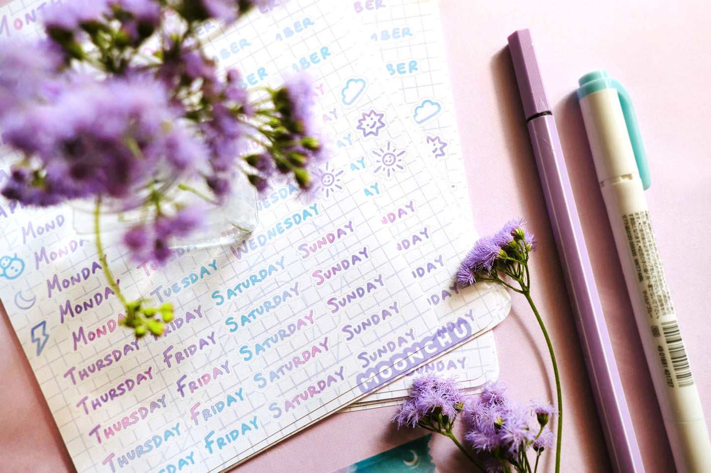 photo depicts original moonchu sticker sheet comprised of colourful uppercase print script (pink, blue, teal, purple gradient). features essential days of the week and months, as well as cute weather icons. a unique kiss cut sticker sheet.