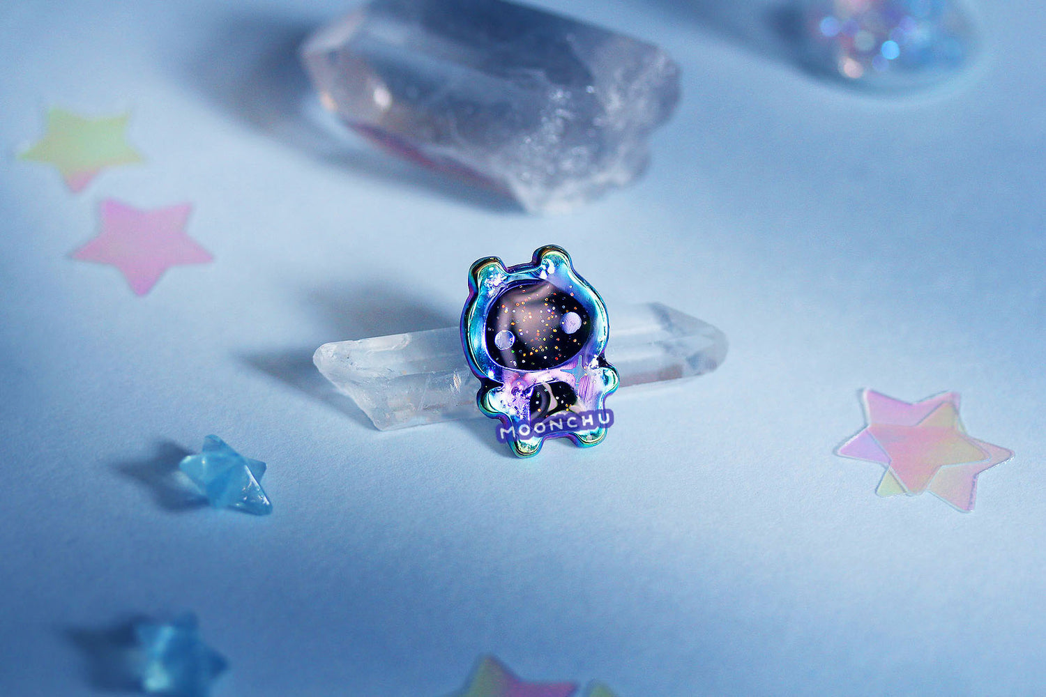 photo depicts moonchu's original art enamel pin of a little alien baby with rainbow anodized metal, holographic twinkling glitter stars, and a glossy finish. a special space galaxy pin.