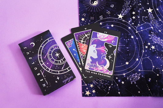 stunning indie holographic tarot deck by moonchu with all original art designs! this photograph depicts the holographic detailed tarot box design, along with the high priestess tarot card. this original artwork showcases two beautiful wolves, one holographic and the other black. they are alternating facing each other, as a crescent moon basks in a river. a magical aura wafts upwards towards a full moon. these are accented delicately in holographic foil.
